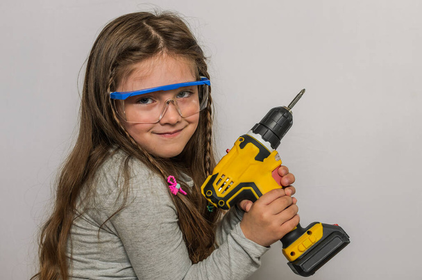 Klein charmant meisje kind glimlachen in veiligheidsbril met een elektrische schroevendraaier - Foto, afbeelding