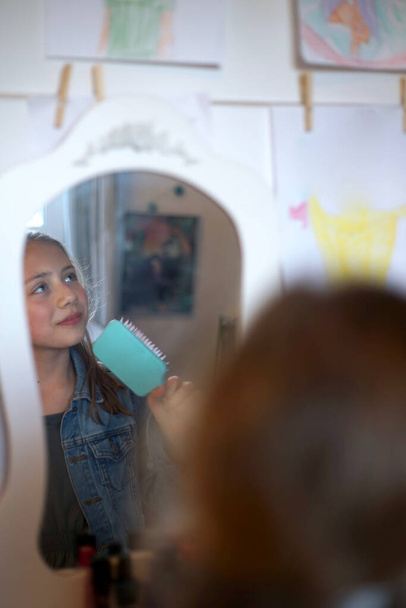 Egy fiatal lány portréja, amint a tükör előtt énekel a hajkeféjével a hiúsági asztalánál.. - Fotó, kép