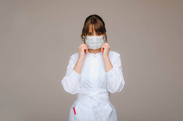 A girl doctor stands in a medical mask, isolated on a gray background - Foto, Imagem