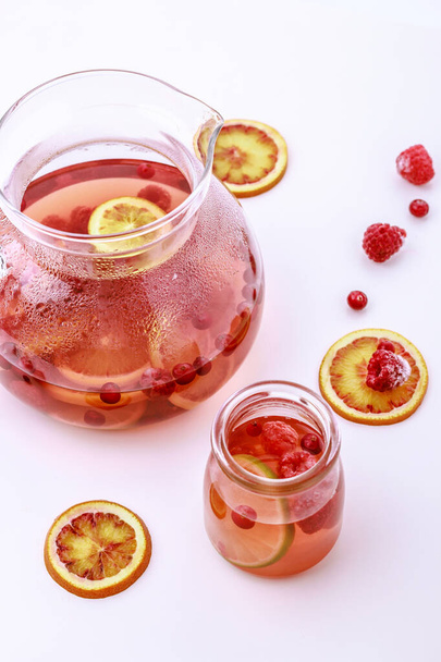 Healthy hot fruit drink. Fruit hot tea with the addition of oranges, lemons and raspberries in a glass cups and teapot on a white table. - Zdjęcie, obraz