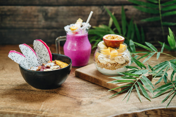 Breakfast Smoothie, Muesli with yoghurt and tropical fruit at brown background and smoothie bowl at the wooden background - Fotó, kép