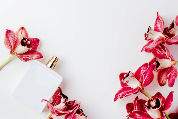 Draufsicht, flache Lage einer weißen Parfümflasche, umgeben von Orchideenblüten auf weißem Hintergrund. Markenlose Parfümflasche.  - Foto, Bild