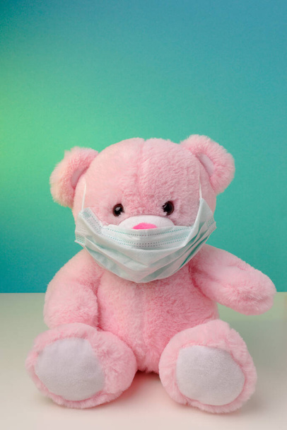 Розовый плюшевый медведь, сидящий в медицинских масках на синем фоне, концепция защиты от вируса и индивидуальный респиратор
 - Фото, изображение