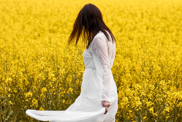 Молодая женщина в белом платье крутится в желтых цветах рапса. Концепция свадебных фотографий с копировальным пространством. Наслаждаясь жизнью
 - Фото, изображение
