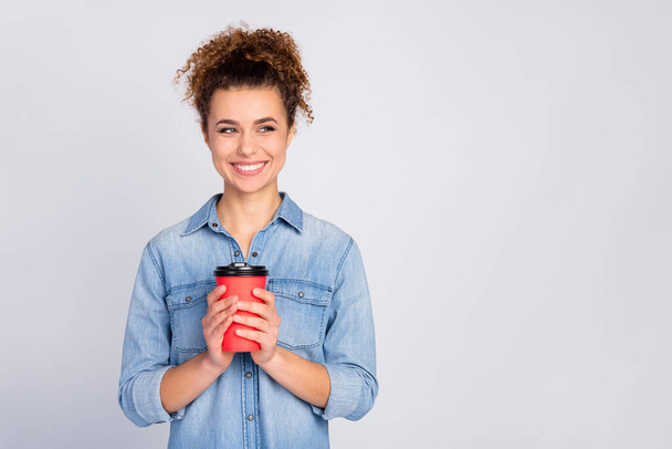 Photo of pretty wavy hairdo lady hold hands red paper takeout coffee mug good mood look empty space wear casual denim blue shirt isolated grey color background - Foto, afbeelding
