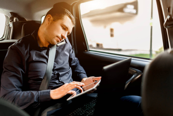 Drukke zakenman in een taxi. Multitasking concept. Passagier rijdt op de achterbank en werkt tegelijkertijd. Spreekt op een smartphone en gebruikt een laptop en tablet. - Foto, afbeelding
