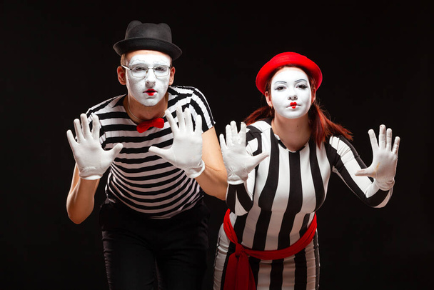 Portrait of man and woman mime artists performing, isolated on black background. Mimes in striped clothes pretending to be behind the glass - Zdjęcie, obraz