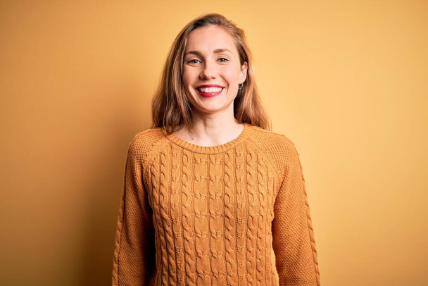 Young beautiful blonde woman wearing casual sweater standing over yellow background with a happy and cool smile on face. Lucky person. - 写真・画像