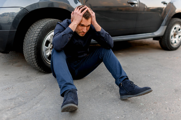 Car accident, traffic accident, a man in despair sits near the wheel of his car. He put his hands on his head. He feels panic and tantrum - Foto, imagen