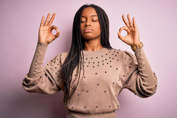 Pembe izole edilmiş arka plan üzerine moda kazağı giyen genç Afro-Amerikalı kadın rahatla ve parmaklarıyla meditasyon hareketi yaparken gözleri kapalı gülümse. Yoga konsepti. - Fotoğraf, Görsel
