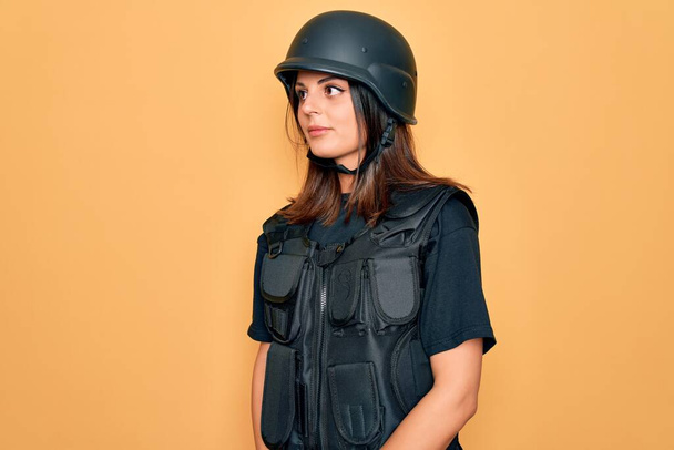 Genç, güzel, esmer asker kadın kurşun geçirmez giysisi ve güvenlik kaskı takıyor. Yan tarafa bakıyor, rahat profil pozu veriyor, kendine güvenen bir gülümsemesi var.. - Fotoğraf, Görsel