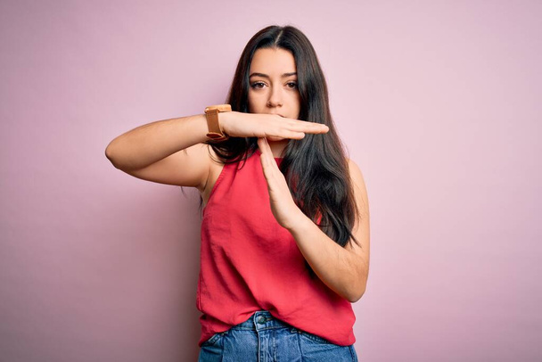Young brunette woman wearing casual summer shirt over pink isolated background Doing time out gesture with hands, frustrated and serious face - Photo, Image