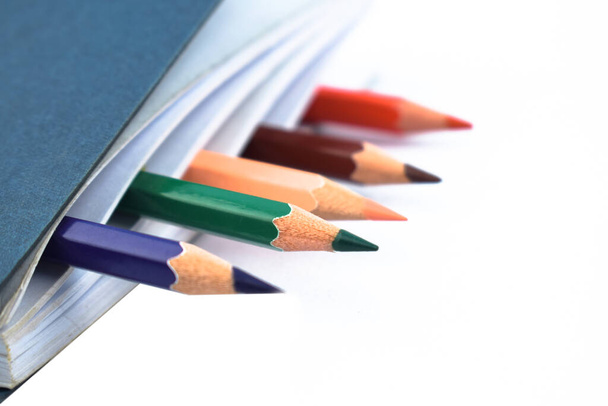 Pięć różnych kolorowych kredek ołówkowych drewna umieszczone w prostym białym notebooku papieru - Zdjęcie, obraz