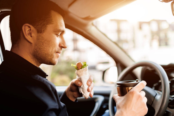 Je m'arrête manger un morceau. Homme manger une collation dans la voiture et boire du café ou du thé
. - Photo, image