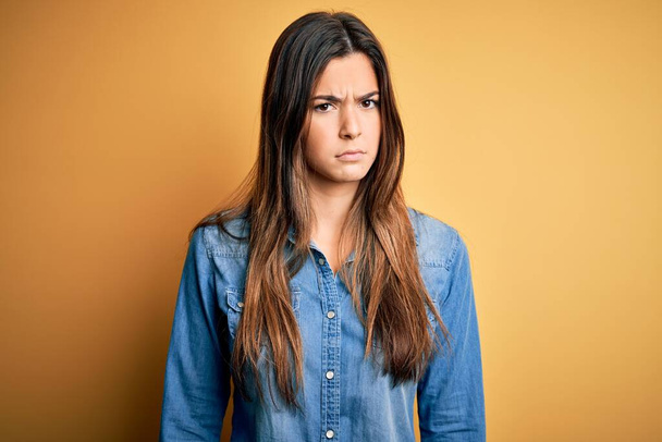 Young beautiful girl wearing casual denim shirt standing over isolated yellow background skeptic and nervous, frowning upset because of problem. Negative person. - Photo, Image