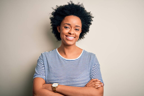 Young beautiful African American afro woman with curly hair wearing striped t-shirt happy face smiling with crossed arms looking at the camera. Positive person. - Photo, Image