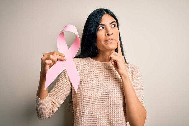 Junge schöne hispanische Frau mit Brustkrebs Bewusstsein rosa Schleife ernstes Gesicht über Frage nachdenken, sehr verwirrte Idee - Foto, Bild