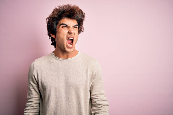 Young handsome man wearing casual t-shirt standing over isolated pink background angry and mad screaming frustrated and furious, shouting with anger. Rage and aggressive concept. - 写真・画像