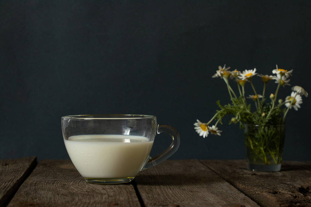 glass of milk and wild daisies on a table in the morning - Фото, изображение