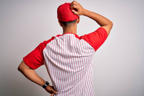 Young handsome african american sportsman wearing striped baseball t-shirt and cap Backwards thinking about doubt with hand on head - Photo, image
