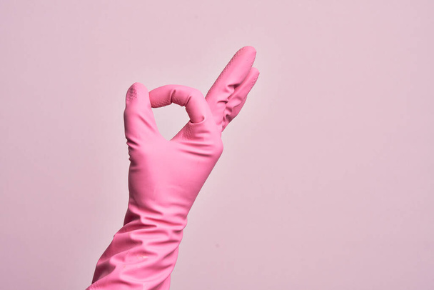 Hand van Kaukasische jonge man met schoonmaak handschoen over geïsoleerde roze achtergrond gebaren goedkeuring expressie doet het goed symbool met de vingers - Foto, afbeelding
