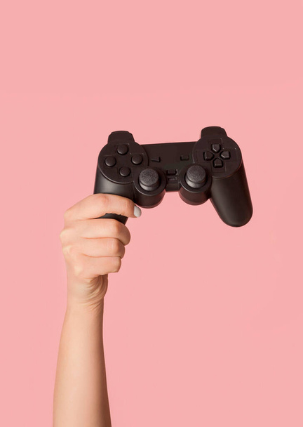Blijf thuis. Vrouwelijke hand tonen video game console op roze achtergrond, close-up - Foto, afbeelding