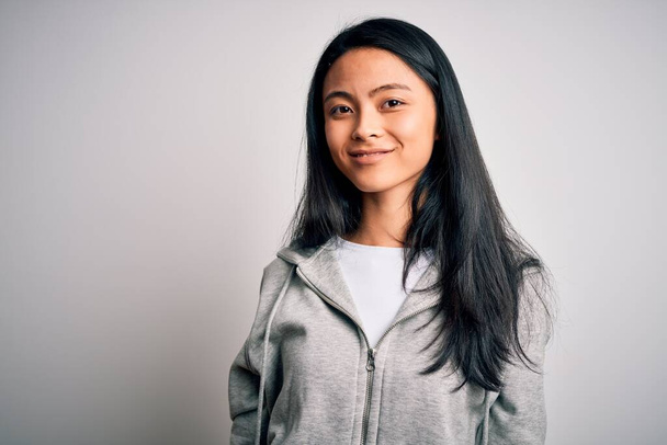 Young beautiful chinese sporty woman wearing sweatshirt over isolated white background looking away to side with smile on face, natural expression. Laughing confident. - Fotó, kép