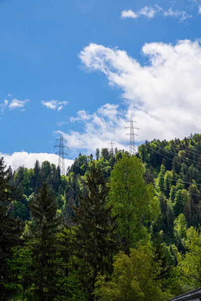 γραμμές ηλεκτρικής ενέργειας υψηλής τάσης και πλέγμα σταυρό σε όλο το δάσος και τα βουνά κάτω από το γαλάζιο του ουρανού στις Ελβετικές Άλπεις με αντίγραφο χώρο - Φωτογραφία, εικόνα