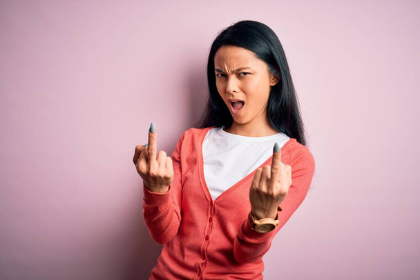 Young beautiful chinese woman wearing casual sweater over isolated pink background Showing middle finger doing fuck you bad expression, provocation and rude attitude. Screaming excited - Фото, зображення