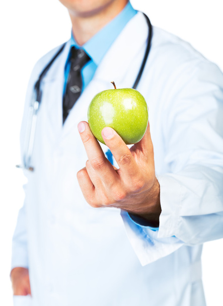 Рука доктора держит свежее зеленое яблоко крупным планом на белом
 - Фото, изображение