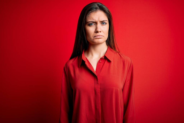 Young beautiful woman with blue eyes wearing casual shirt standing over red background skeptic and nervous, frowning upset because of problem. Negative person. - Foto, Imagem