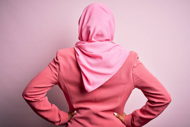 Nuori afrikkalainen afro nainen yllään muslimi hijab yli eristetty vaaleanpunainen tausta seisoo taaksepäin katsellen pois kädet kehon
 - Valokuva, kuva