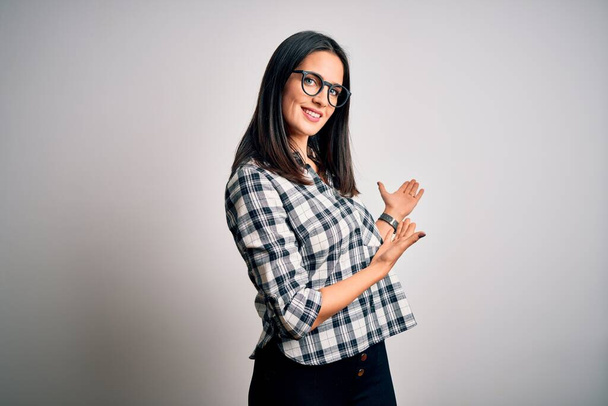 Young brunette woman with blue eyes wearing casual shirt and glasses over white background Inviting to enter smiling natural with open hand - Photo, Image