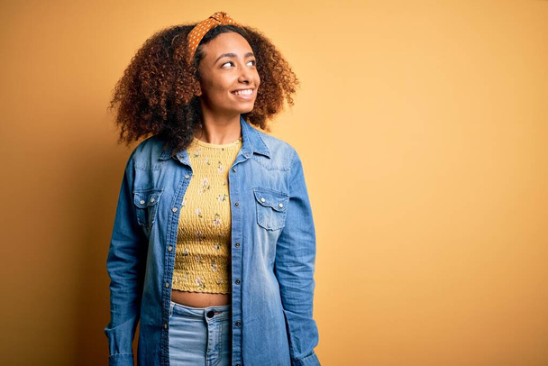 Beautiful african american with afro hair standing over yellow isolated background looking away to side with smile on face, natural expression. Laughing confident. - Foto, Imagen