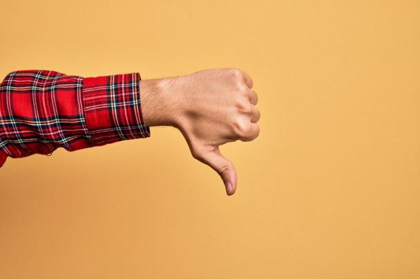 Mão de jovem caucasiano mostrando dedos sobre fundo amarelo isolado fazendo polegares para baixo gesto de rejeição, desaprovação antipatia e sinal negativo - Foto, Imagem