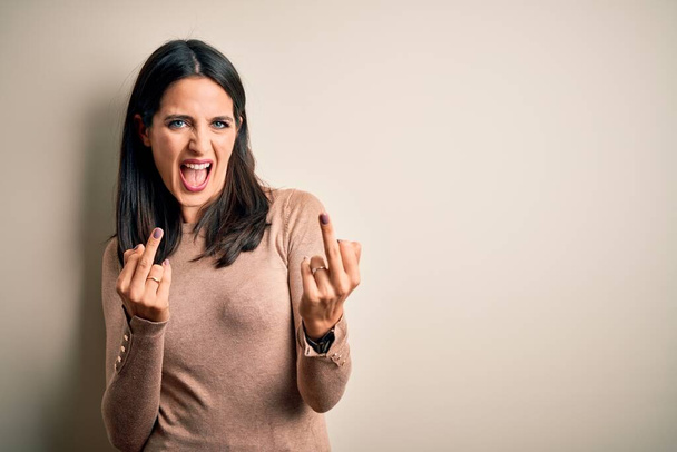 Young brunette woman with blue eyes wearing casual sweater over isolated white background Showing middle finger doing fuck you bad expression, provocation and rude attitude. Screaming excited - Φωτογραφία, εικόνα