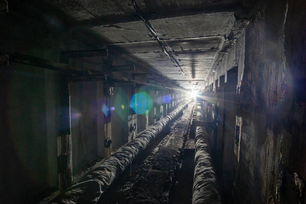 Underground concrete utility tunnel with pipes and wires. Utility tunnel with light in the end. - Photo, Image