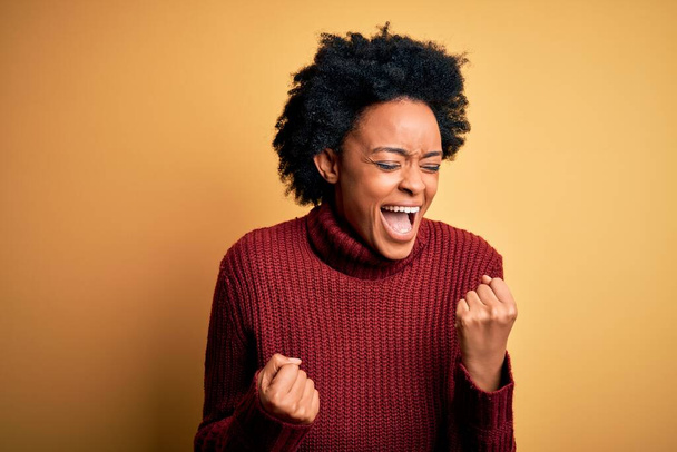 Young beautiful African American afro woman with curly hair wearing casual turtleneck sweater celebrating surprised and amazed for success with arms raised and eyes closed. Winner concept. - Foto, Imagen