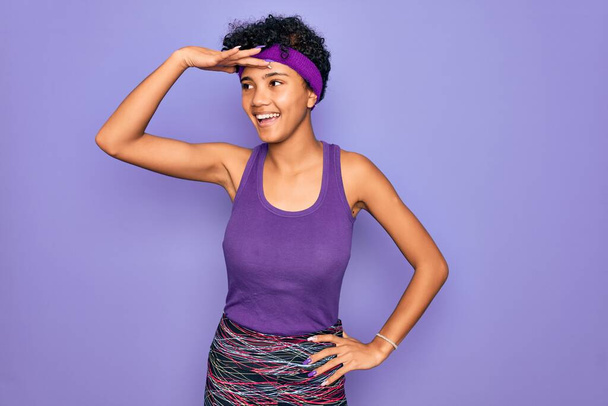 Beautiful african american afro woman wearing casual sportswear over purple background very happy and smiling looking far away with hand over head. Searching concept. - Valokuva, kuva