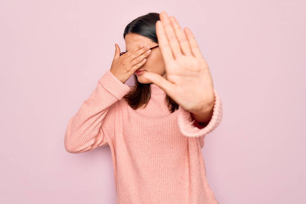 Jonge mooie brunette vrouw dragen casual trui en bril over roze achtergrond bedekken ogen met handen en doen stop gebaar met droevige en angst uitdrukking. Beschaamd en negatief concept. - Foto, afbeelding
