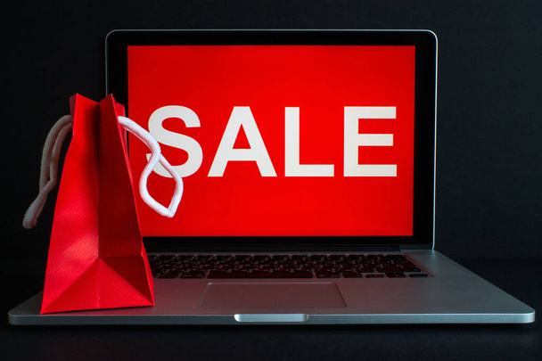Κόκκινη χάρτινη σακούλα για κοντινό πλάνο στον υπολογιστή και η επιγραφή στην οθόνη - πώληση σε φωτεινό φόντο. Η έννοια των online αγορών - Φωτογραφία, εικόνα