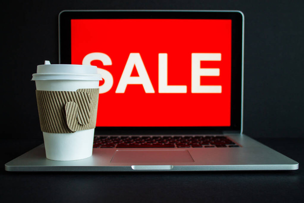 A disposable Cup of coffee on the computer close-up and the inscription on the screen - sale on a bright red background. The concept of online shopping and delivery - Zdjęcie, obraz