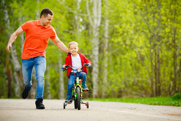 Father help his son ride bicycle in sunny day park - 写真・画像