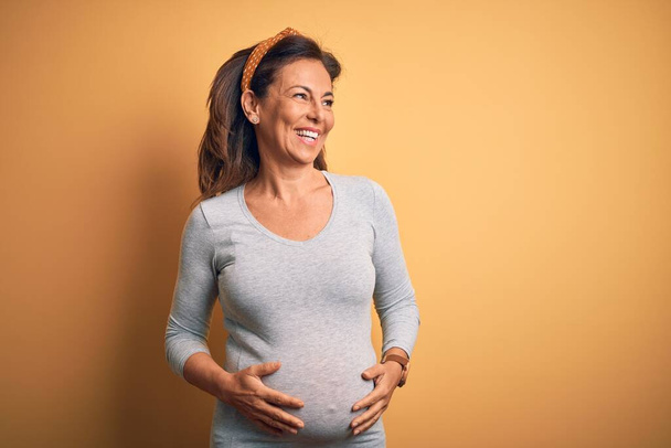Schwangere mittleren Alters, die ein Baby im Alter der Schwangerschaft erwartet, schaut mit einem Lächeln im Gesicht, natürlichem Ausdruck zur Seite. Zuversichtliches Lachen. - Foto, Bild