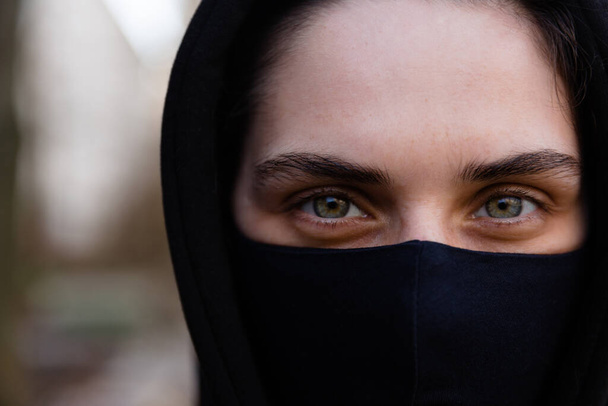 Young woman wearing face mask. Handsome woman in black hoodie wear black medical mask. Close up portrait. Pandemic coronavirus covid-19 quarantine period concept. - Photo, Image