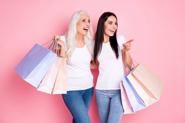 Portrait of two nice attractive lovely pretty cheerful cheery glad women embracing carrying buyings pointing look dream idea isolated over pink pastel color background - Foto, immagini