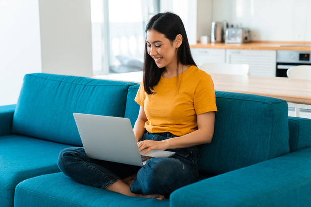 Photo of a beautiful happy cheerful brunette young woman on sofa indoors at home using laptop computer. - Fotografie, Obrázek