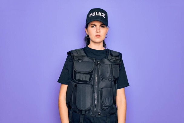 Egy fiatal rendőrnő golyóálló mellényt visel lila háttér felett, álmos és fáradt, kimerült fáradtság és másnaposság miatt, lusta szemek reggel.. - Fotó, kép