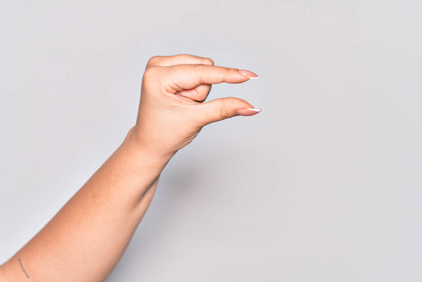 Mano de mujer joven caucásica recogiendo y tomando cosa invisible, sosteniendo el objeto con los dedos mostrando espacio - Foto, imagen