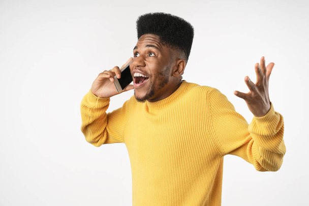 Handsome excited man expressing surprise on face and gesturing while speaking on telephone isolated over white background - 写真・画像